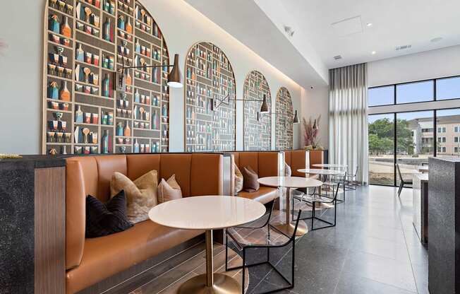 A modern restaurant with a long table and chairs, a large window with a view of buildings outside, and a wall with a pattern of bottles.