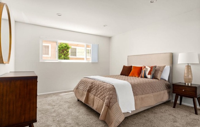 A bedroom with a bed, nightstand, lamp, and a mirror on the wall.