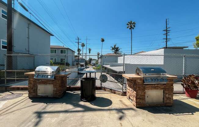 two bbq pits in a yard with a fence and buildings