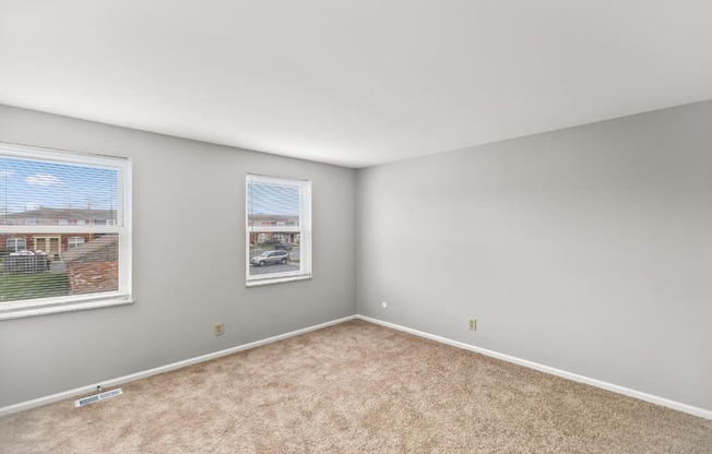 A room with a carpeted floor and a window showing a view of a residential area.