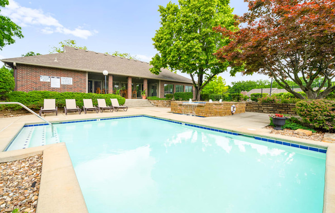 A swimming pool in front of a house with trees.