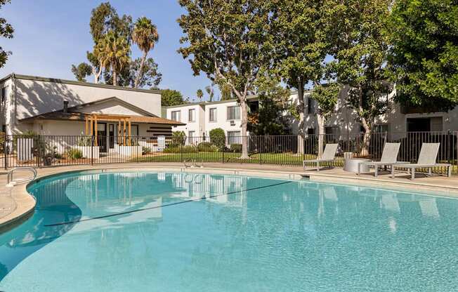 A swimming pool in front of a house with trees in the background.