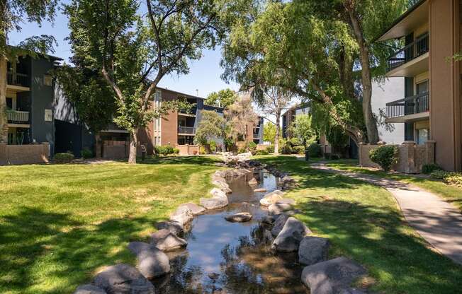 a stream runs through a grassy area between two apartment buildings