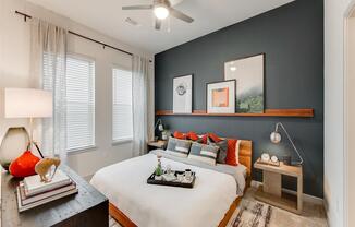 Apartments Grapevine - Stylish Bedroom With Dark Gray Accent Wall and Three White Walls, Two Large Windows, Silver Ceiling Fan, and Modern Furnishings