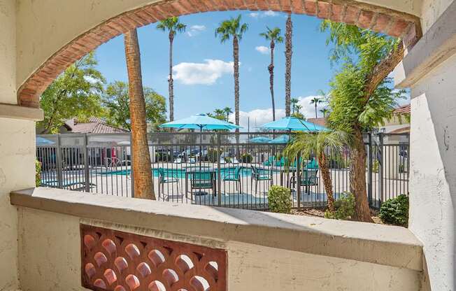 A view from a window looking out at a pool surrounded by palm trees.