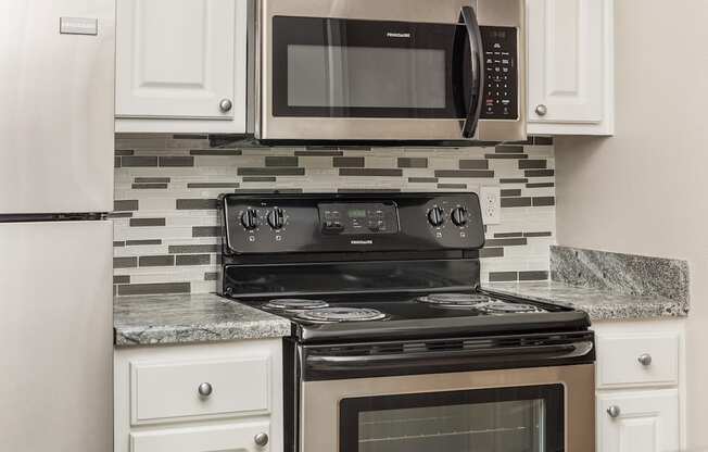 a kitchen with a stove and microwave and white cabinets at Highland Ridge Apartments, Overland Park 