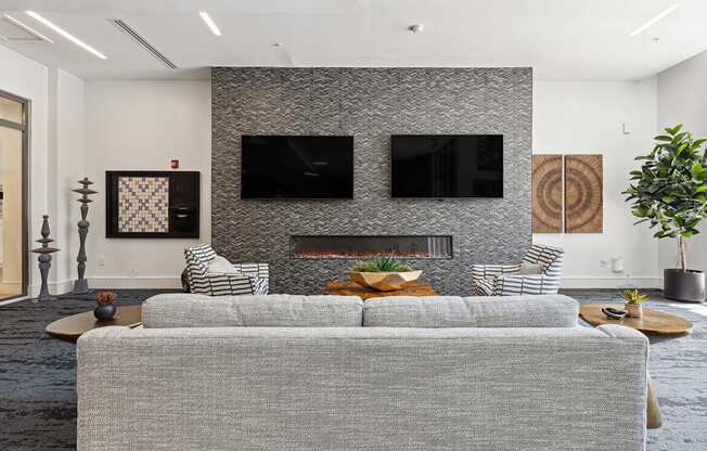 a living room with a gray couch and two televisions on the wall