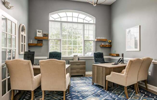 A room with a desk and chairs with a window in the background.
