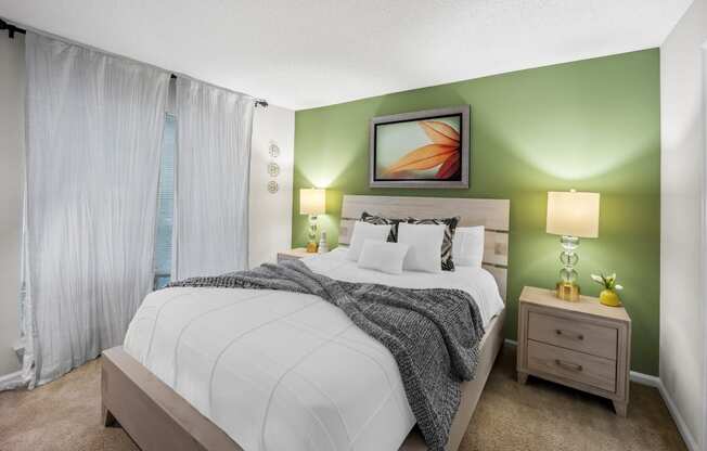 Furnished bedroom with green accent wall and white bedding and curtains at University Ridge Apartments, Durham, NC, 27707