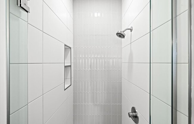 A white tiled shower with a glass door and a silver handle.