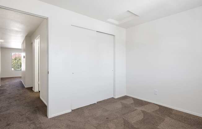 a living room with white walls and carpet and a door to a hallway