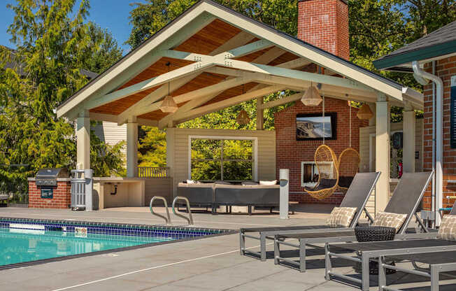 A poolside patio with a covered seating area and a brick chimney.