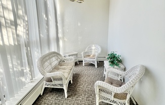 Charming sunroom with white wicker furniture and soft carpeting, basking in natural light.