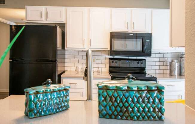 A black refrigerator and microwave in a kitchen with white cabinets.