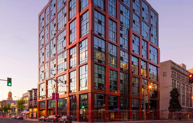 A tall red building with many windows stands in the middle of a street.