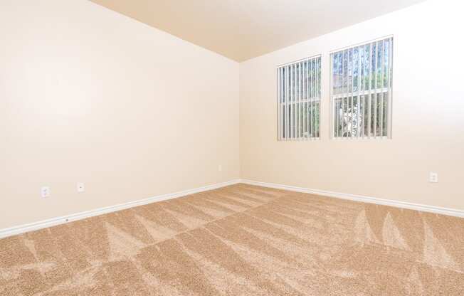 a bedroom with beige carpet and two windows
