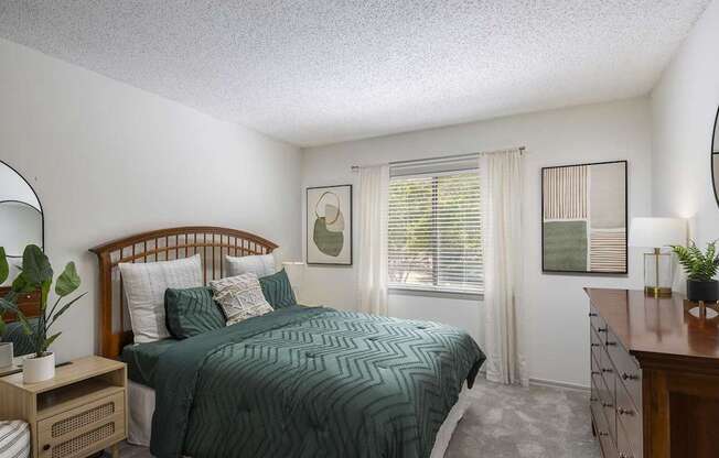 A bedroom with a bed, nightstand, and window.