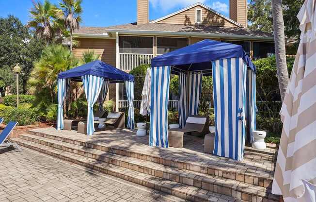 Two blue and white striped canopies are set up on a brick patio.