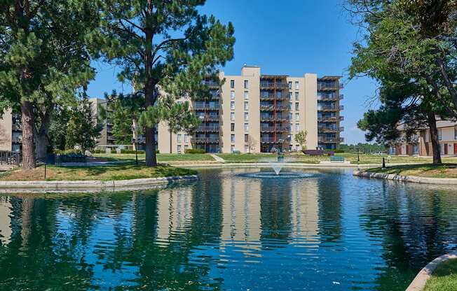 A pond in front of a residential building surrounded by trees.