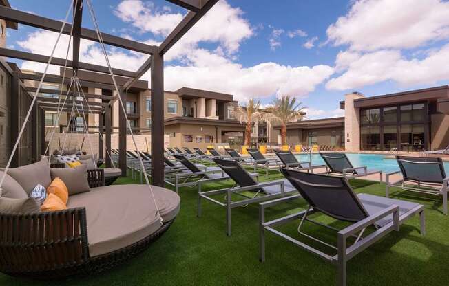 A sunny day at the poolside with lounge chairs and a hanging chair.