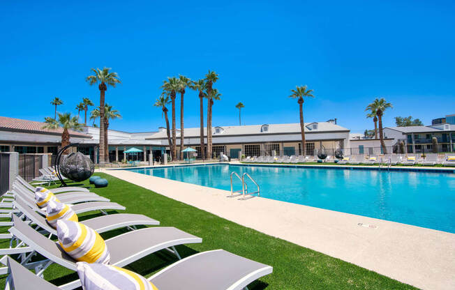 a resort style pool with white chairs and palm trees at Presidio Palms Apartments, Tucson