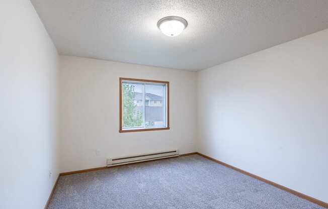 the living room of an empty room with carpet and a window. Fargo, ND Oxford Apartments