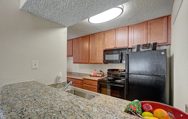 A bright kitchen at Acacia Park featuring warm wood cabinetry, granite-style countertops, black appliances, and an efficient open layout with overhead lighting that makes everyday cooking feel easy and comfortable.