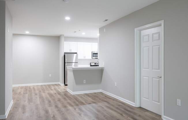 an empty living room with a kitchen in the background