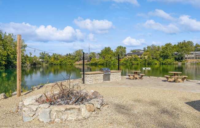 a fire pit next to a lake with picnic tables