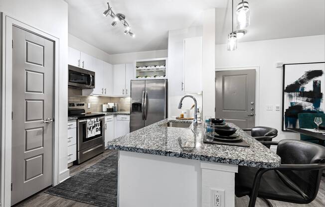 Upgraded gourmet kitchen featuring granite countertops with designer backsplash and stainless steel appliances at Cyan Craig Ranch apartments for rent