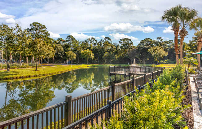 A serene park with a lake, trees, and a wooden fence.