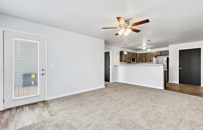 a living room with a ceiling fan and a kitchen in the background