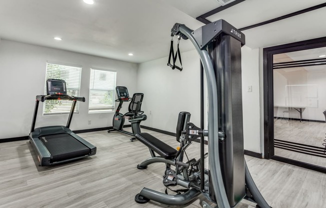 a gym with exercise equipment in a home with white walls and wood floors