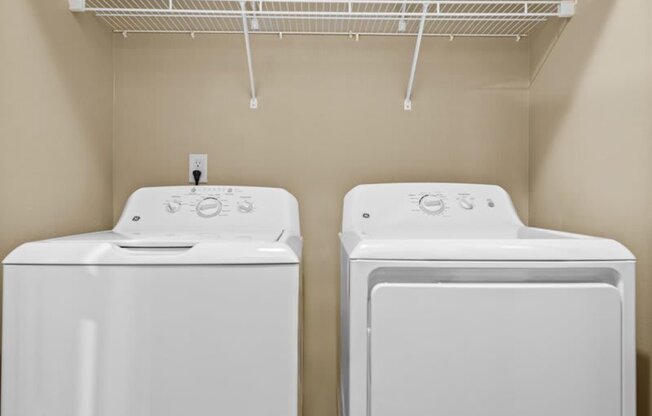 two washers and dryers in a laundry room with a rack on the wall