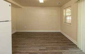 A room with a white fridge and wooden flooring.
