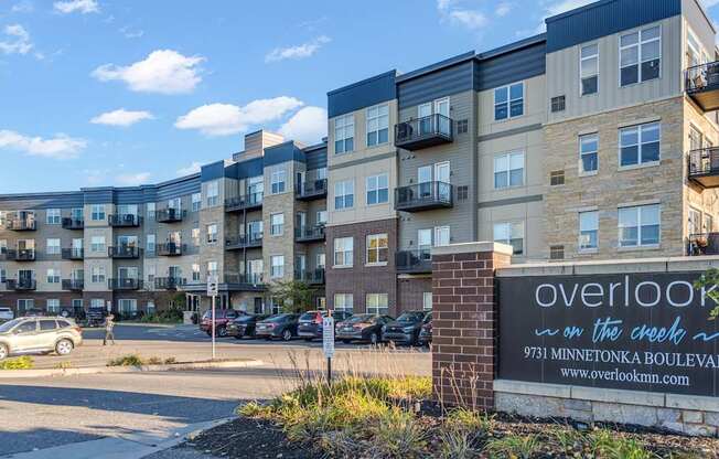 The image shows a multi-story residential building with a sign in front that reads