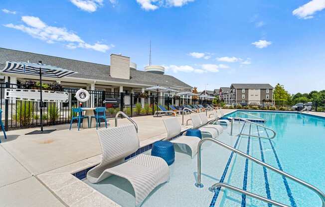 A swimming pool with blue water and white lounge chairs.