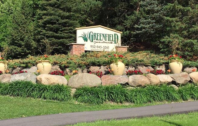 Outdoor property sign atop grass and large rocks that reads "Greenfield"