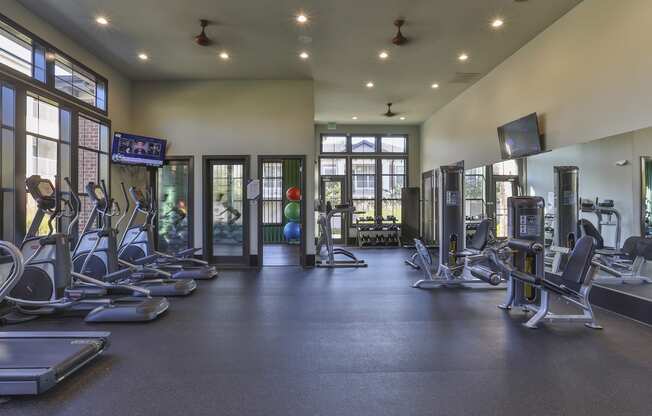 the fitness center has cardio equipment and weights in a large room with windows