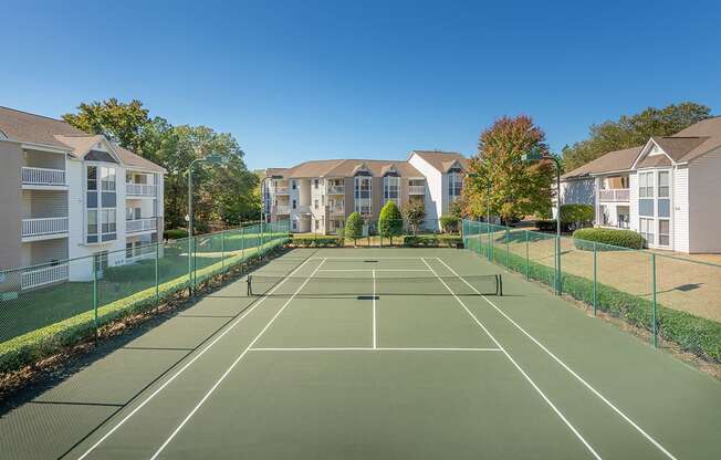 A tennis court is surrounded by apartment buildings.