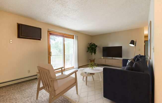 Bismarck, ND Brandon Apartments. A living room with a couch and a chair. A large sliding glass door allows natural light to fill the room.