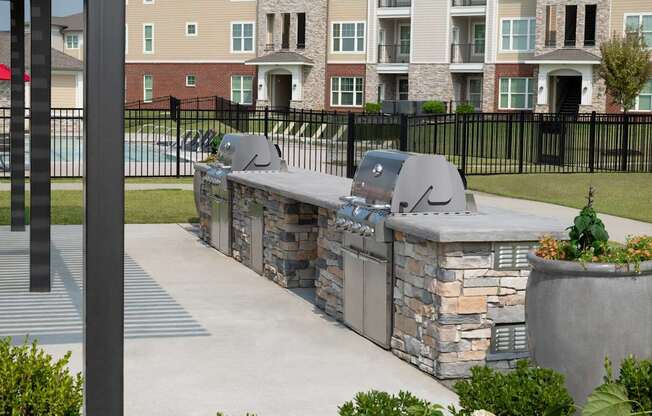 A stone barbecue grill is in the middle of a concrete patio.