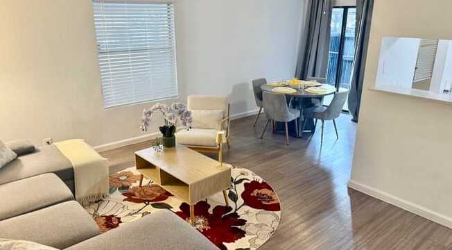 A living room with a grey sofa, a coffee table, and a dining table set up.