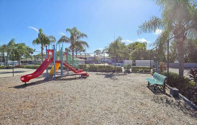A playground with a red slide and green bench.