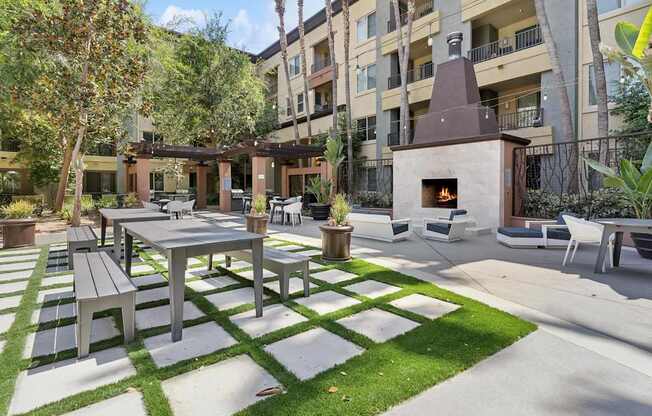 A patio with a table and chairs is surrounded by a grassy area and apartment buildings at The Kitt at Warner Center Apartments, Woodland Hills
