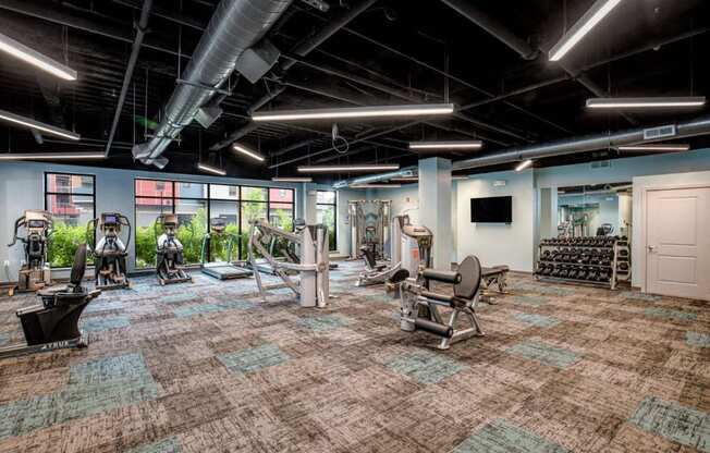a gym with weights and cardio equipment in a large room with windows