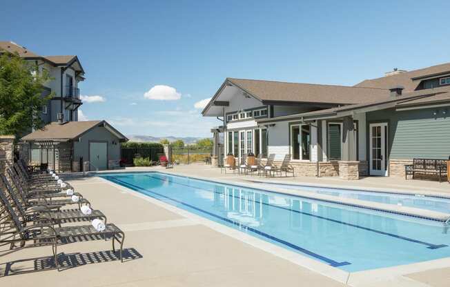 a swimming pool with chairs around it in front of a house