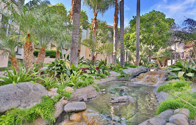 A small waterfall in a garden surrounded by green plants.