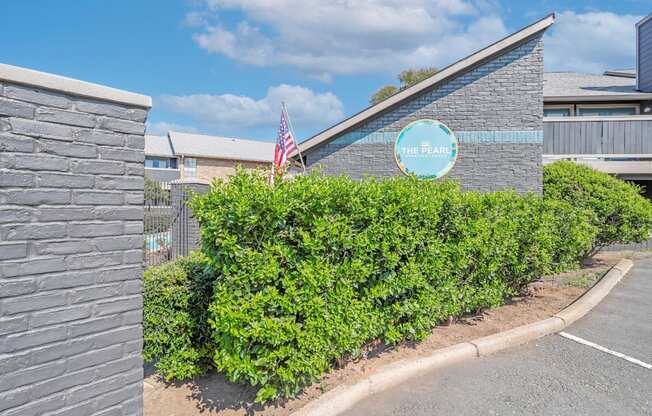 A building with a sign that says "The Pearl" is surrounded by green bushes.