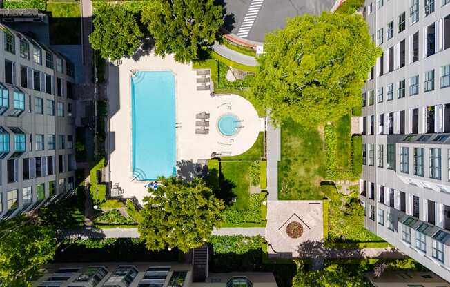 A swimming pool is surrounded by trees and grass in a courtyard.